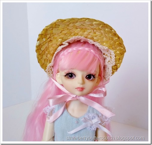 The front view of a pink haired bjd wearing a pretty bonnet.