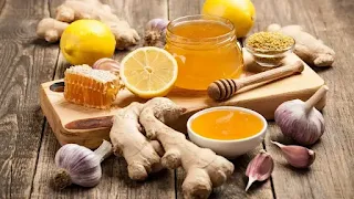 كوب زجاجي مليء بشاي الثوم مع العسل، محاط بفصوص الثوم الطازجة وملعقة من العسل، مشروب صحي مثالي لتعزيز المناعة وتحسين الهضم.