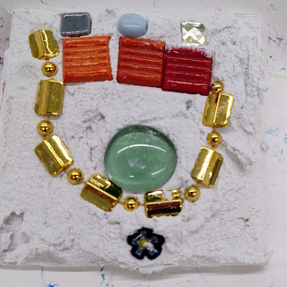 various small glass pieces and beads sit amidst grout in a child's tile mosaic at ArtSplash 2022
