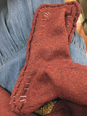 The foot of a single garnet-red hose (looking rather brick-red in this photo) with dense pins pointing upward from the edge of the sole, where they're holding the folded-over edge of the seam allowance.