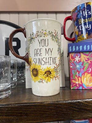 A photo of a tall coffee mug with a sunflower on it and the words: you are my sunshine.