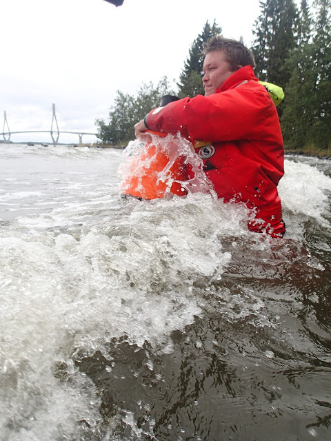 Pelastautumispukuinen henkilö taistelee aaltoa vastaan vesikiikarin kanssa meressä