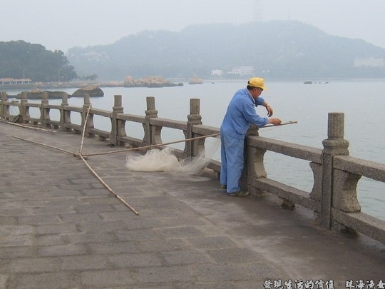 老伯正在賣力的用著組合這竹竿與漁網簡單自製的捕魚工具。