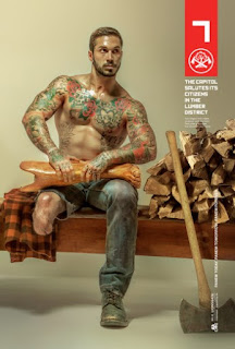  A foto mostra o modelo Alex Minsky, ex-fuzileiro naval que lutou no Afeganistão. Alex está sentado em um banco de madeira, à direita, próximo a ele, uma pilha de achas de lenha e o cabo de um enorme machado encostado na pilha. Alex é um homem de pele bronzeada, rosto oval, cabelos curtos castanhos claros, sobrancelhas levemente arqueadas, nariz reto, lábios médios, bigode e barba por fazer; está desnudo da cintura para cima evidenciando uma tatuagem colorida que envolve os torneados braços, musculoso peito e o bem definido abdômen; ele segura a parte inferior de uma perna mecânica sobre as coxas; perna esquerda com calça jeans surrada e sapato gasto e parte do joelho direito a mostra com a parte da calça cortada acima do joelho. À esquerda, sobre o assento, uma camisa xadrez em ocre, marrom e preto.