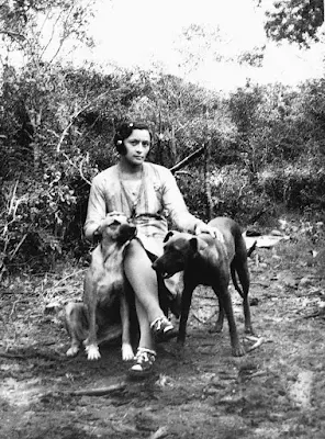 Foto de Maria Bonita, a cangaceira, sentada numa cadeira ao lado de uma cachorro