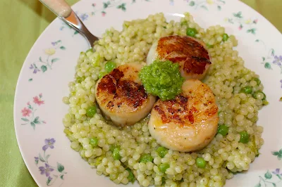 Finished plate of seared scallops over pearl couscous with peas and garlic scapes.