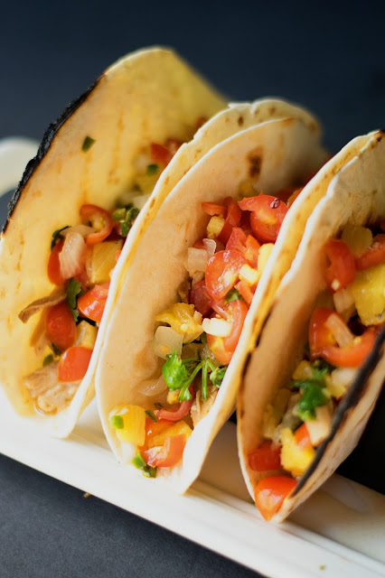 Three tacos, in a holder, on a plate, fully assembled.