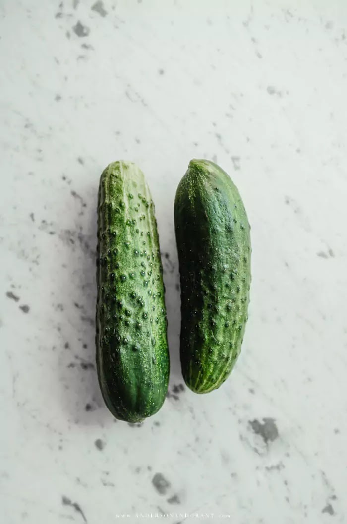 Two pickling size cucumbers on marble countertop