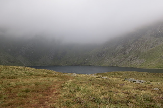 A dark, glacial lake overhung by low cloud.