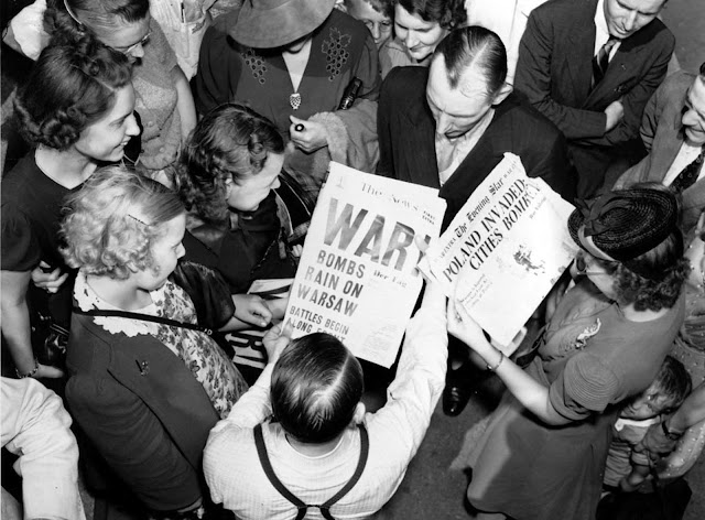 A crowd reads newspaper headlines, 