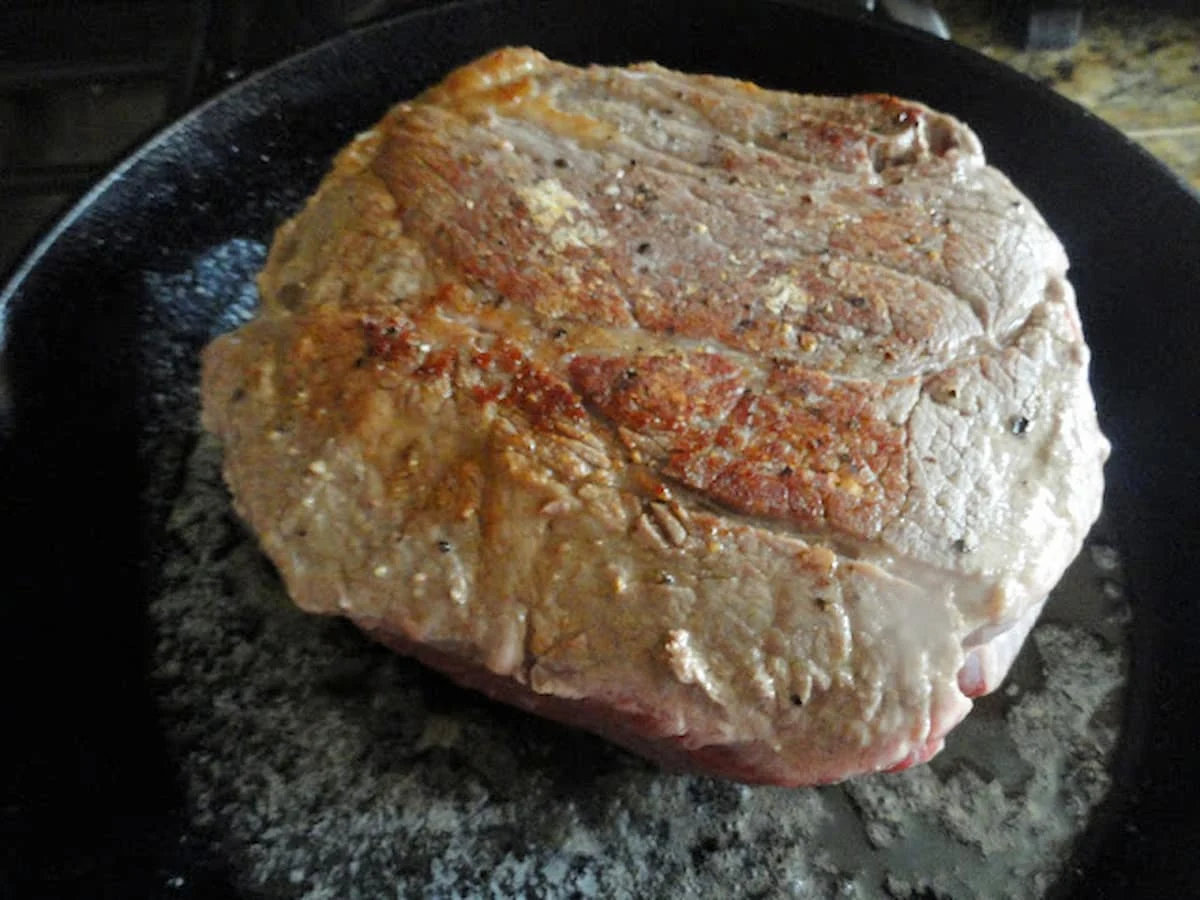 A beef chuck roast being browned in a cast iron pan.