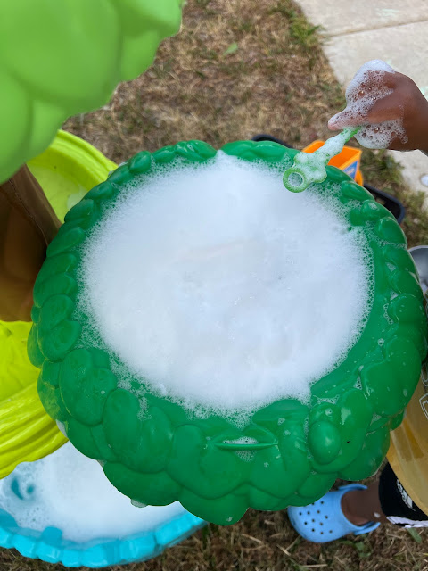 a child's hand playing with bubbles in a water table.