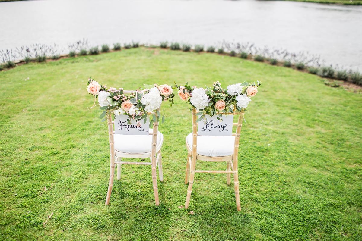 two wedding chairs on a grenn grass close to the lake