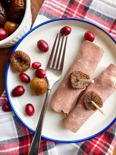 Figs, fresh cranberries and beef roll ups on a blue rimmed white plate with fork.