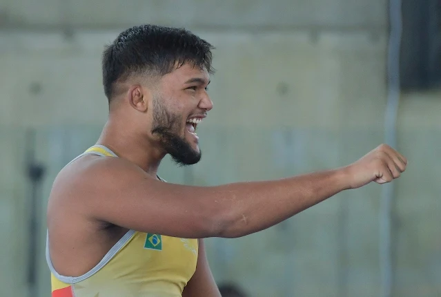 Igor comemora após vencer a semifinal do wrestling em Cali. Ele veste uma malha amarela e estica um braço para frente, dando um soco no ar