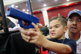 Young child using a lethal firearm with the encouragement of his father.