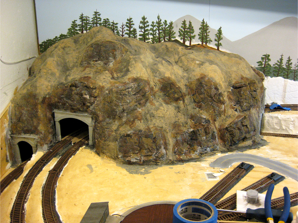 A wash of thinned black acrylic paint being applied to plaster hard shell terrain and plaster rock outcroppings