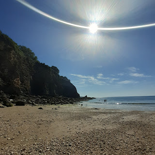 Long shot of beach with tall cliffs, low tide, soft sand, sun light making a smiley arc in the blue sky