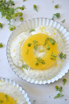 Helle Creme in einem Dessertschüsselchen, darauf eine Scheibe Ananas und bestreut mit Blütenköpfchen und Blättchen der Strahlenlosen Kamille.