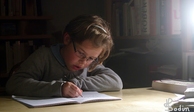 Petite fille écrit, concentrée à son bureau.