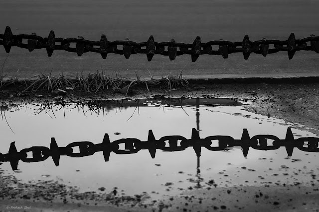 A Black and White Minimal Art Photograph of the Reflection of a Metal Chain in Water.