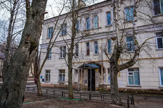 Двойные узкие окна в подъезде Трехэтажный дом за голыми деревьями
