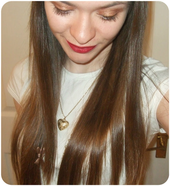 girl with long brown hair looking down wearing gold heart necklace and shimmery bronze eyeshadow and red lipstick