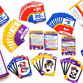 A number of stacks of colourful cards of various types, some containing icons, some containing text, and some containing numbers with mathematics operators like plus and minus signs.