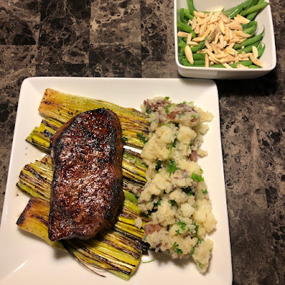 Grilled New York strip on a bed of grilled leeks with some smashed red potatoes with butter and parsley and haricots verts almondine