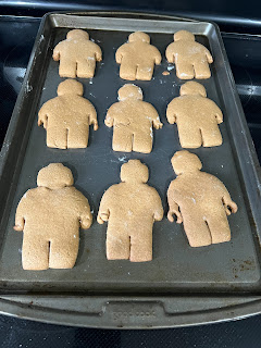 9 gingerbread cookies shaped like lego mini figures fresh out of the oven, still on a cookie sheet