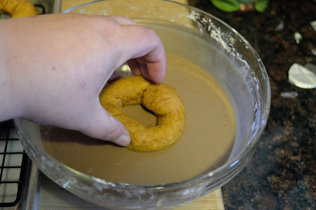 A pumpkin donut being dipped into the glaze. 