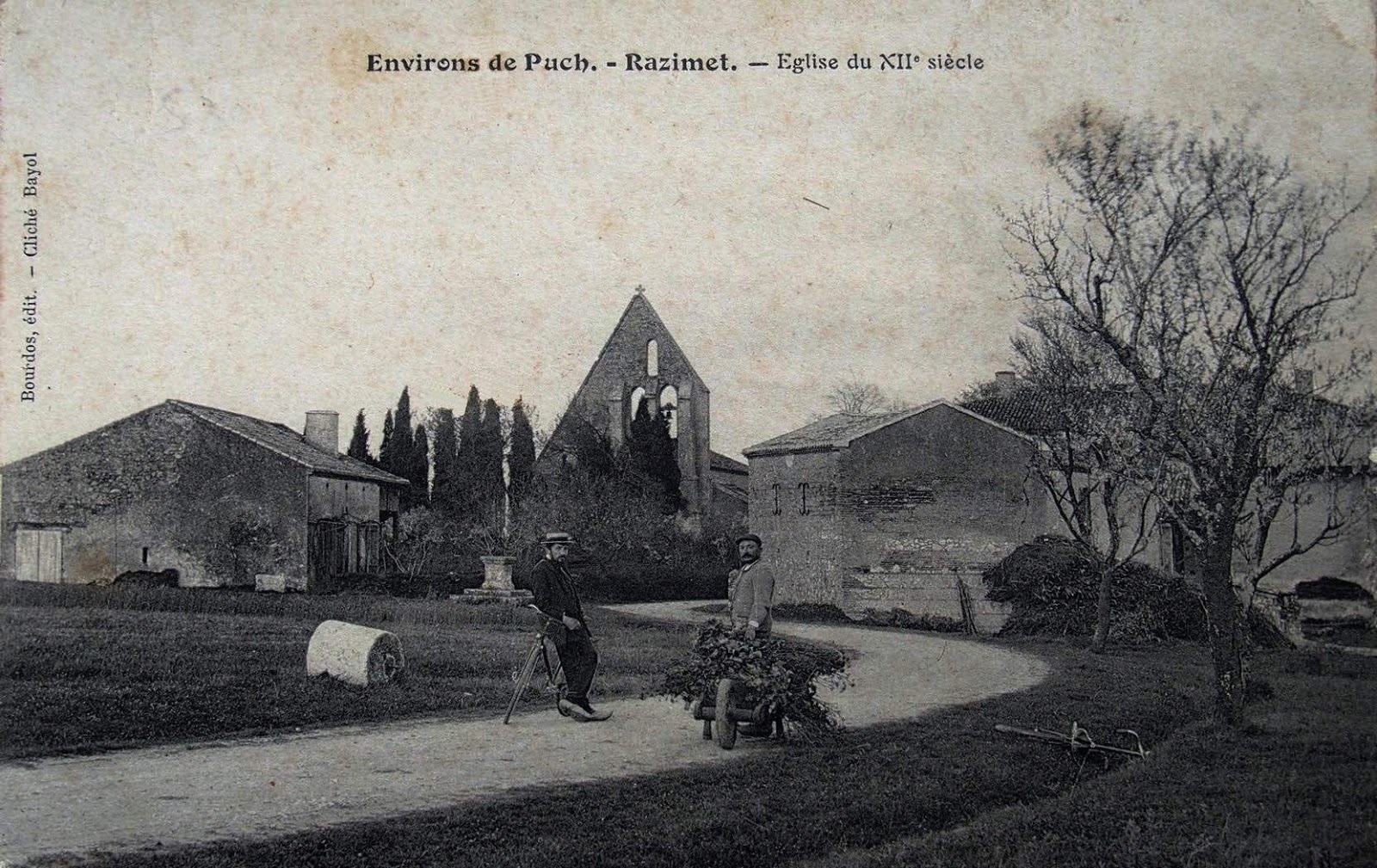 carte postale ancienne de l'entrée bourg de Razimet, l'instituteur appuyé sur son vélo devise avec le paysan devantysa brouette, en fond l'église