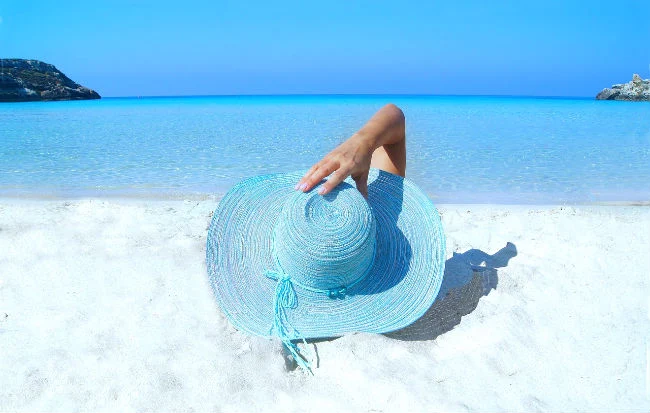 Donna con cappello di paglia sulla spiaggia sotto il sole