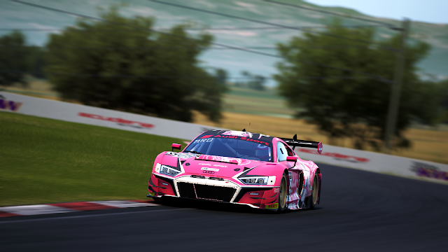 Picture from Assetto Corsa Competizione: an Audi R8 LMS evo II painted in the Queens' Design colours. It is pink with matte black and glossy white accents. On the sides is Victoire Laviolette, the team's mascot.