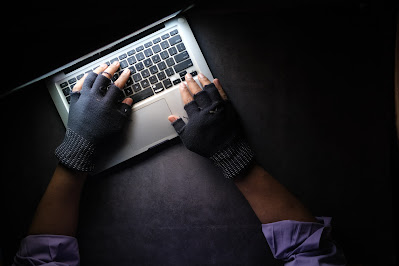 Persona tecleando en un portátil con mitones en un entorno oscuro, iluminado únicamente por la pantalla