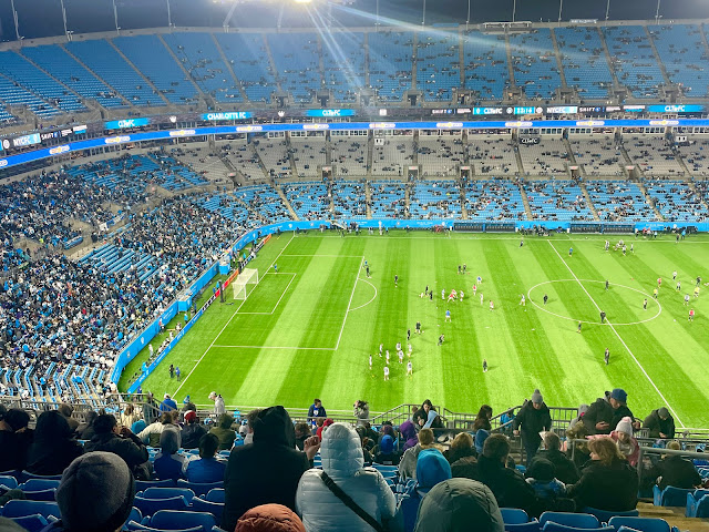 FC Charlotte players are warming up on the field below. The stadium is only partially full.