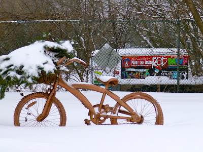 Cheery orange bike with basket of snow-covered greenery in front of Paint the Town Red trailer, Marina Park, Port Credit.