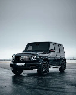 A Mercedes-Benz G-Wagon, showcasing its distinctive boxy design and off-road capabilities, surrounded by scenic nature on an open road."