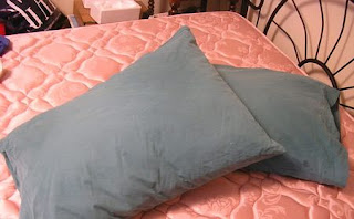 Two pillows, with green pillowcases remade from an old duvet cover lay on a bed mattress.