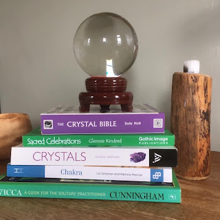 Crystal ball sat on a pile of green, blue and white witchcraft books