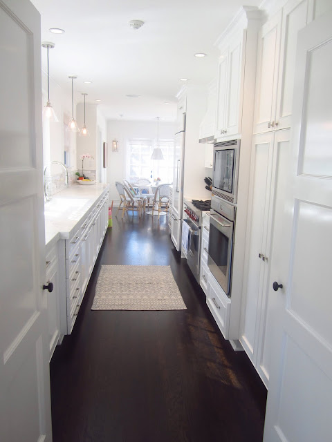 Galley kitchen with white counters and cabinets and dark wood floors