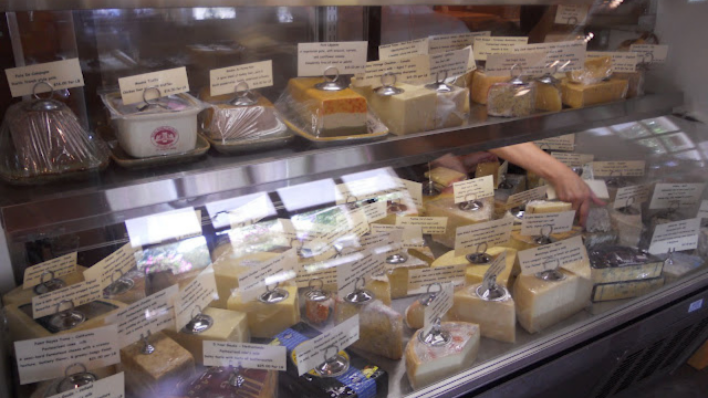 A display case full of different cheeses at a cheese shop.