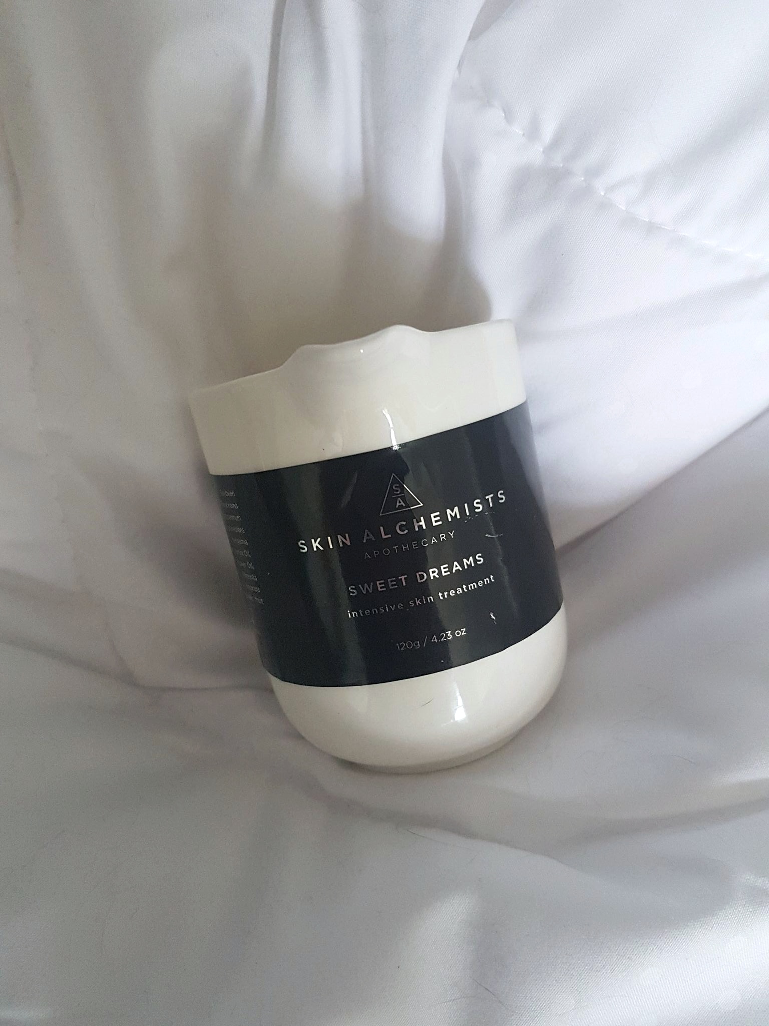 Skin Alchemists Intensive Skin Treatment Massage Candle on a white duvet