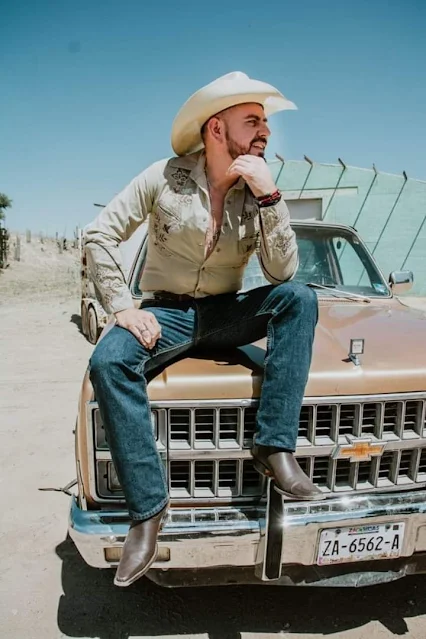 10/11 sitting on the hood of a Cadillac out in the desert a cowboy wearing blue jeans and brown tan grey leather cowboy boots