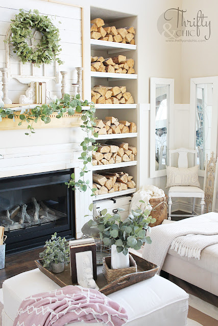 living room with white couch, large window, stacked wood, and shiplap mantel