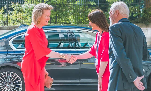 Queen Mathilde wore an orange Adria asymmetric jumper by Natan, and orange Milan trousers from Natan. Gold earrings