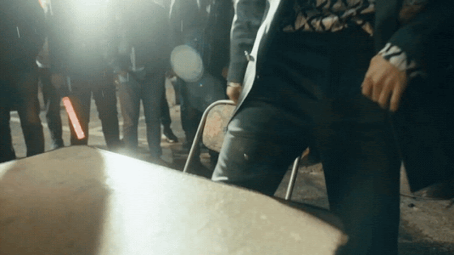 Gif from the music video for Seventeen Hip-Hop sub-unit song "Lalali" where Wonwoo dressed up as a mobster sits on a table and prepares to wrestle a thing made from metal