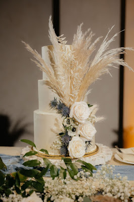 three tier white wedding cake with blue flowers and pampas grass