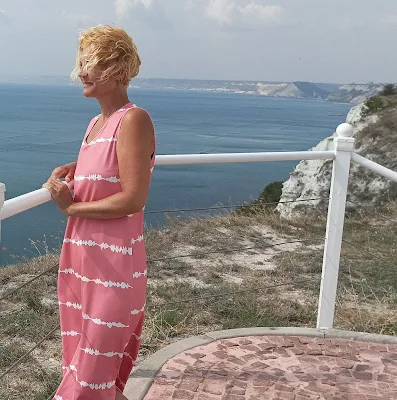 blonde girl with long pink dress staring at the sea
