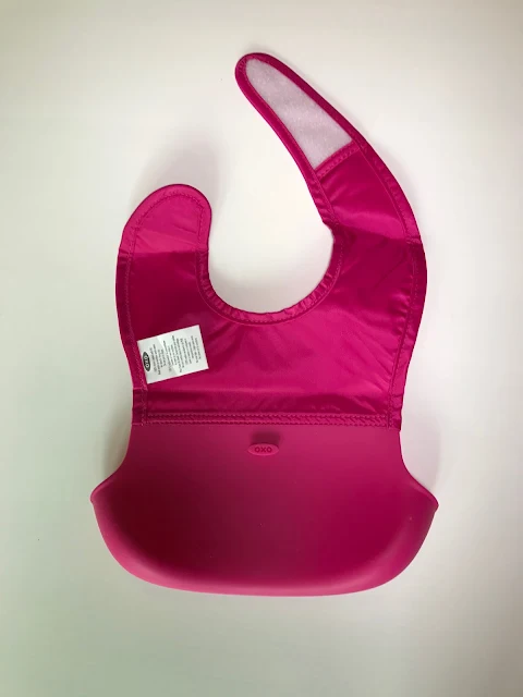 View of the back of the pink bib showing a long section of white velcro to secure it around a child's neck